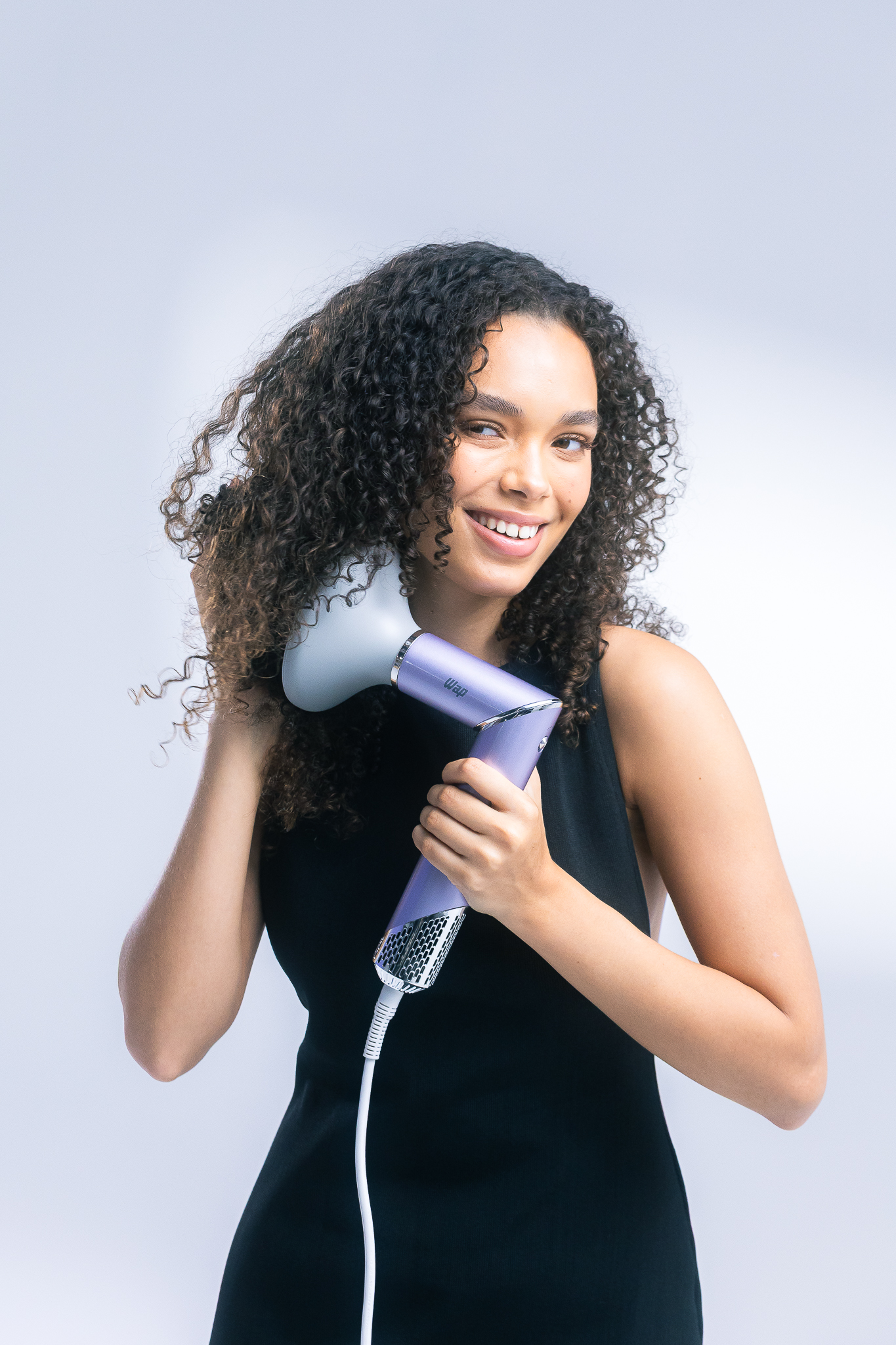 Mulher de cabelo cacheado sorrindo enquanto usa o secador WAP com difusor